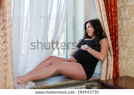 Pregnant woman  sits near window in the room.