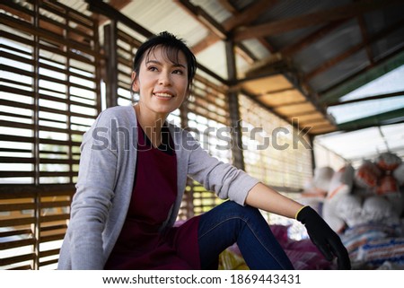 Portrait of confident Asian gardener owner woman sitting on fertilizer at farm workplace , Small business entrepreneur concept