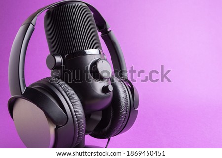 Black professional recording microphone with headphones on a orange background, side view