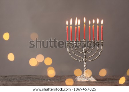Silver menorah with burning candles on table against grey background and blurred festive lights, space for text. Hanukkah celebration