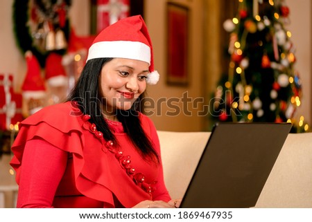 Mature women in Christmas cap using Laptop waving sipping coffee at home on Christmas eve
