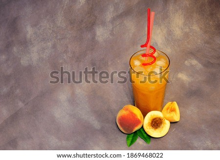 A glass of orange peach juice with ice, straws next to ripe fruits on a gray background. Close-up.