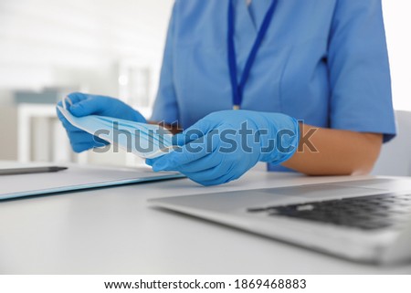 Doctor in medical gloves holding protective mask at table in office, closeup