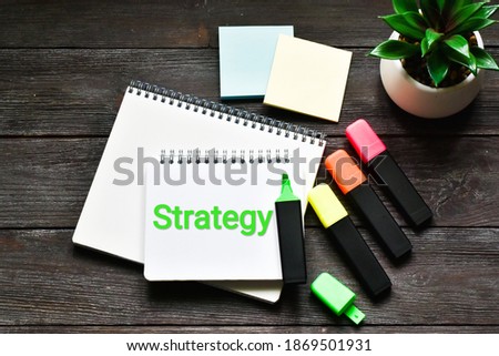 Strategy. Green plant, a markers next to a notebook that says STRATEGY on a wooden table. Flat lay. Business and finance concept.