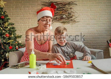 A Little boy with grandmother make Christmas craft, greeting card. Christmas tree and decoration on background.