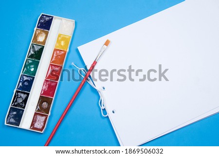 Paint brush and album. Flat lay composition for drawing on blue background. Blank page for text or picture, children mockup