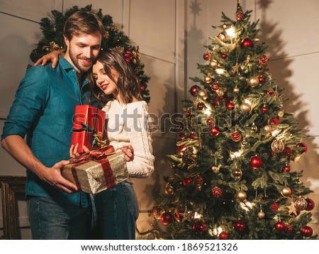 Smiling beautiful woman and her handsome boyfriend. Happy cheerful family posing in the interior near Christmas tree. Models hugging. Love, x-mas concept. They holding gift boxes for each other