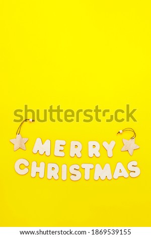 Text Merry Chritmas made from wooden letters on yellow background, vertical format