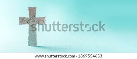 Stone cross with inscription Believe on grey background, Copy space. Christian backdrop. Biblical faith, gospel, salvation concept. Banner. Royalty-Free Stock Photo #1869554653