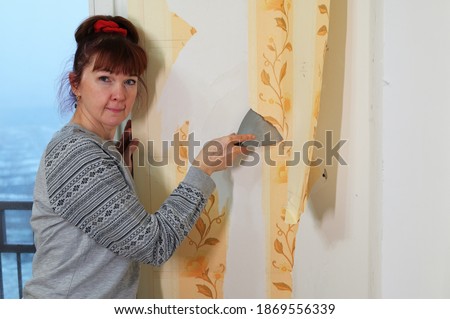 Pretty woman removes wallpaper from the wall in the room. Home renovation photo.