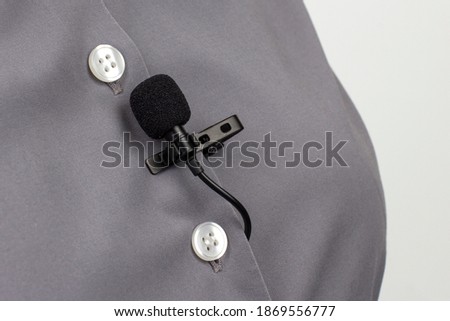 The lavalier microphone is secured with a clip on a gray women's shirt close-up. Audio recording of the sound of the voice on a condenser microphone.