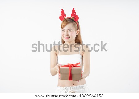 Asian woman is wearing christmas reindeer antlers holding big giftbox in hands grey background.