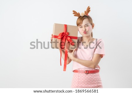 Asian woman is wearing christmas reindeer antlers holding big giftbox in hands grey background.