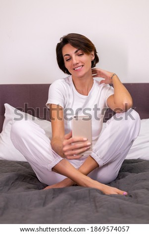 Caucasian woman blogger at home in casual clothes cozy bedroom take photo selfie on mobile phone in mirror