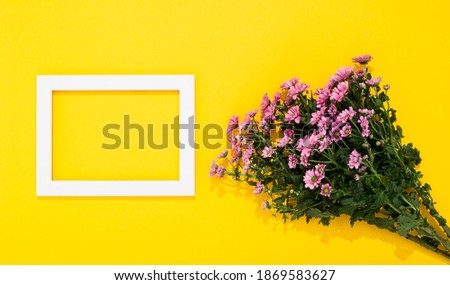 Bouquet of small pink chrysanthemums and white picture frame lays on yellow background with copy space. Holiday or business card. Happy Valentine Day February 14. Woman Day March 8. Mother Day May 8.
