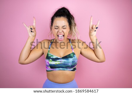 Young beautiful woman wearing sportswear over isolated pink background shouting with crazy expression doing rock symbol with hands up