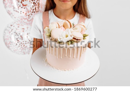 Beautiful happy little girl holding a beautiful big birthday cake, birthday celebration with balloons, over isolated white background