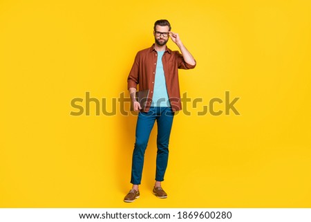 Full length photo of young business man confident serious hold laptop hand touch glasses isolated over yellow color background
