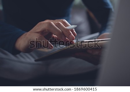 Casual business man with stylus pen touching on digital tablet screen while working on laptop computer in office. Web designer working his project, dark tone, close up. Business, technology concept
