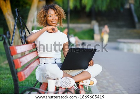 A young female african-american woman working on her laptop computer, enjoying a day at the park