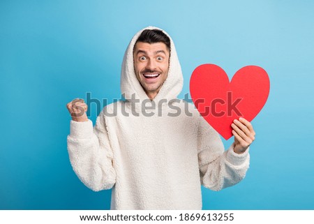 Photo portrait of celebrating man holding big red heart card wearing wool hoodie isolated on pastel blue colored background
