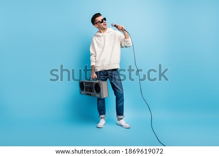 Photo portrait full body view of singing man with stubble carrying boombox holding microphone isolated on pastel blue colored background