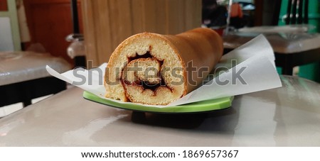 A Fresh Yellow Roll Tart Home Industry Served On A Green Rectangular Plate Just Out Of The Oven Covered With White Baking Paper. Filled With Grape And Strawberry Jam That Is Sweet And Delicious To Eat