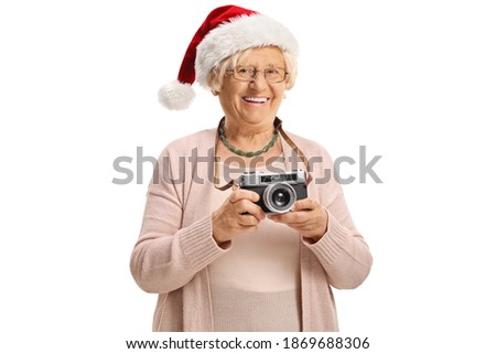 Elderly lady with a vintage camera wearing a santa claus hat isolated on white background
