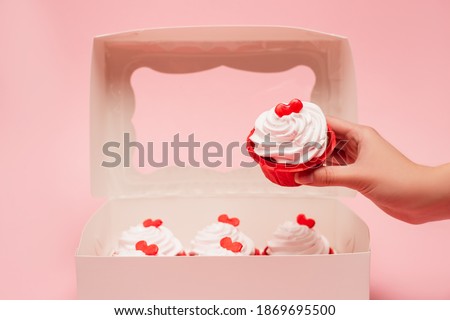 cropped view of woman holding valentines cupcake near box on pink background