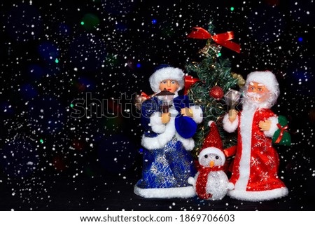 Christmas card with Santa Claus snow Maiden and Snowman on a dark background with snow and flashing lights of garlands. Christmas toy