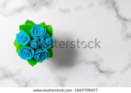 The top view of a toy potted bush of felt roses is on a grey stone  background.  Handmade artificial plants concept. Copy space.