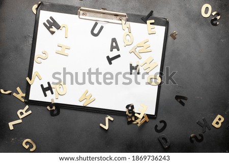 Board with plain white piece of paper on it. Thin wood of letters drop from above.