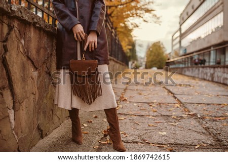 Autumn street fashion details: brown suede bag with fringe in hands of elegant woman wearing stylish outfit. Copy, empty space for text Royalty-Free Stock Photo #1869742615