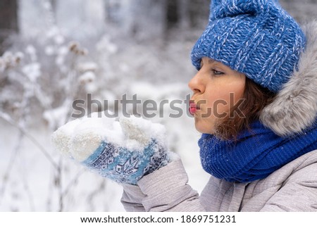 Happy young woman with winter clothes blowing snow.