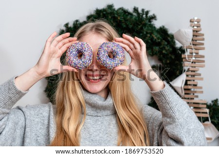 slim blonde woman holding colorful donuts against her eyes and smiling, attractive young woman with long hair having fun with sweets