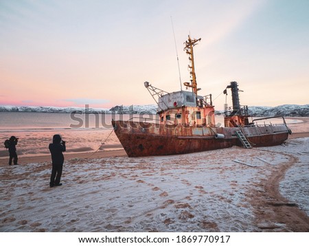 Photographers take photos of a ship washed up on the coast of the Arctic ocean by a storm.