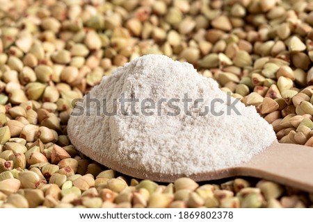 Spoonful of buckwheat flour on top of raw green buckwheat.