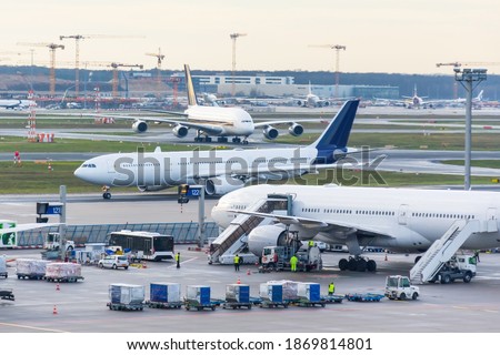 Busy airfield view with airplanes and service vehicles. View of International Airport with planes, gangways, trucks and service equipment. Travel and industry concepts Royalty-Free Stock Photo #1869814801
