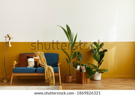 Cozy interior with stylish velvet sofa, wooden cube, carpet, decoration, copy space, a ot of plants and elegant personal accessories. Modern living room in classic house. Template.