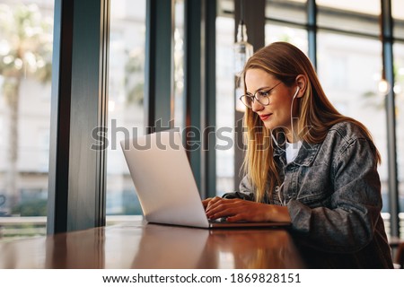 Woman sitting at cafe table and working on laptop computer. Female surfing internet on laptop using cafe wifi. Royalty-Free Stock Photo #1869828151