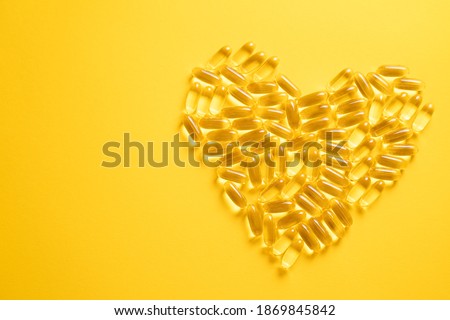Heart shape made of softgel pills, gel capsules, omega, supplement isolated on yellow background Royalty-Free Stock Photo #1869845842