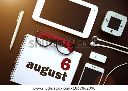 August 6th. Day 6 of month, Calendar date. Office workplace with laptop, notebook, office supplies and stationery on brown back. Summer month, day of the year concept