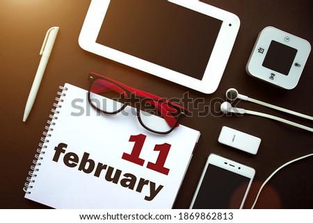 February 11st . Day 11 of month, Calendar date. Office workplace with laptop, notebook, office supplies and stationery on brown back. Winter month, day of the year concept