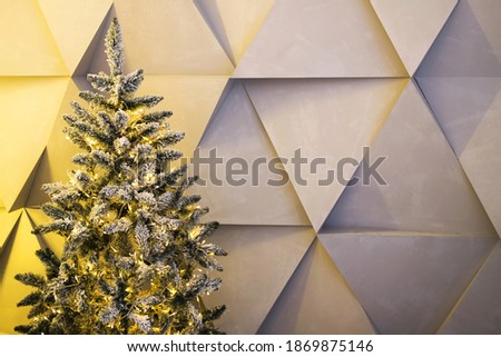 Coniferous tree decorated with fairy lights against gray wall with geometric ornament on Christmas day at home