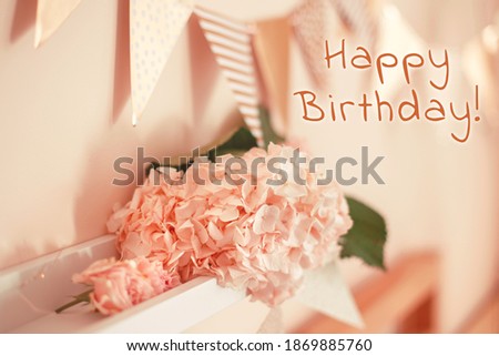 Happy Birthday card with greeting text. Room decoration in pink beige neutral colors for birthday celebration. Macro closeup of light pink hydrangea flowers and triangle flags on shelf for party.