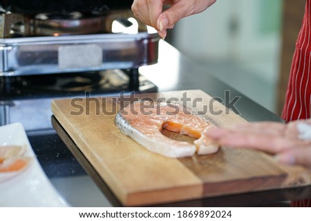 selected focus of wooden cutting board with Asian woman wearing red apron preparing healthy homemade recipe salmon fish in the kitchen.  work from home new normal concept. 