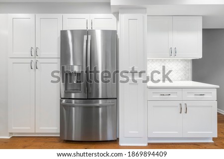 White kitchen built with shaker style cabinets and white quartz countertop. Shows stainless steel appliances, white mosaic tile back splash and  lights.  Royalty-Free Stock Photo #1869894409