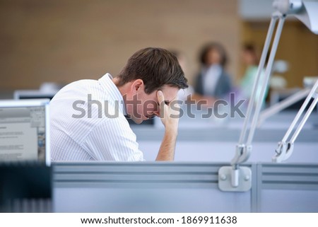 A side profile shot of a stressed businessman looking down with hands on his head in an office cubicle.