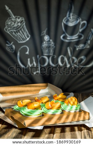 Cupcakes with fruits and berries in a box on a wooden table, a wall with chalk drawings, different light effects. chalk drawings.
