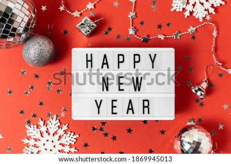Happy new year 2022 table with light box with Christmas silver balls, white snowflakes and confetti.Fun Celebration holiday party time table invitation or greeting card.New year eve concept on red